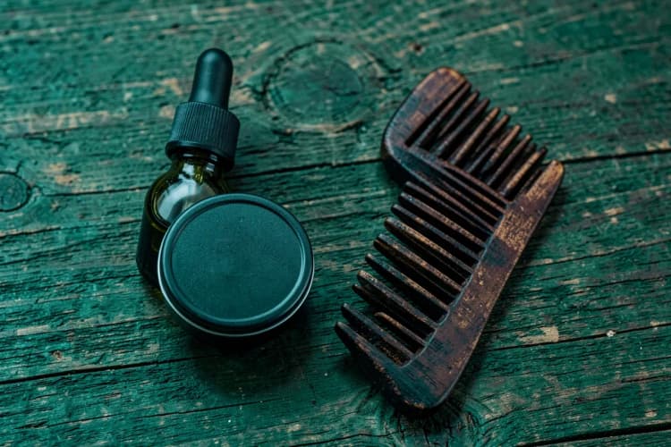 Kit com óleo, balm e pente para barba em embalagens escuras sobre fundo de madeira.