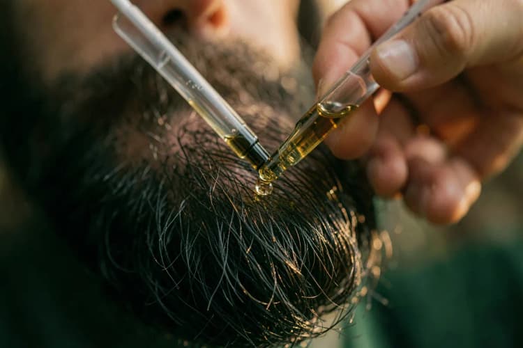 Homem aplicando óleo em sua barba com um conta-gotas.