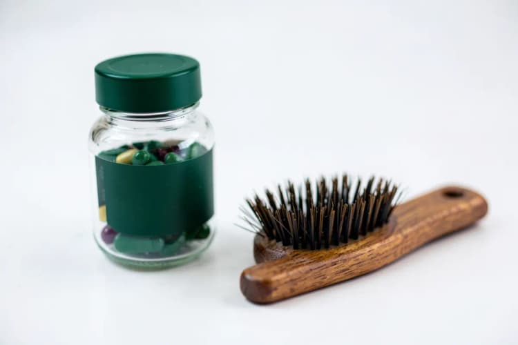 Frasco de suplemento vitamínico ao lado de um pente com cabelo.