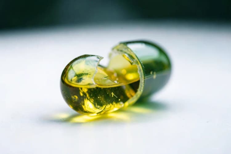 Cápsula de vitamina E quebrada mostrando o óleo dourado dentro.